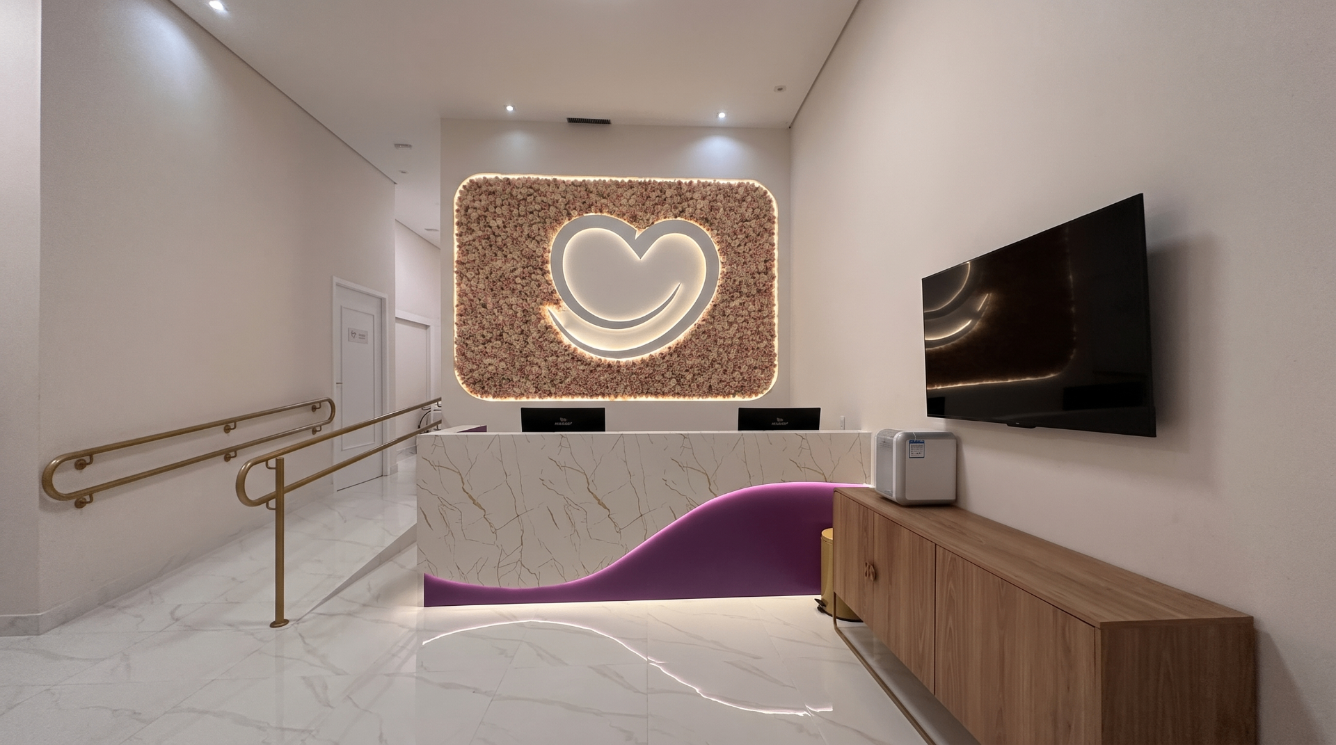 Recepção da nova unidade da Clínica Impla no Shopping Santo Amaro, com painel floral, coração iluminado e balcão de mármore