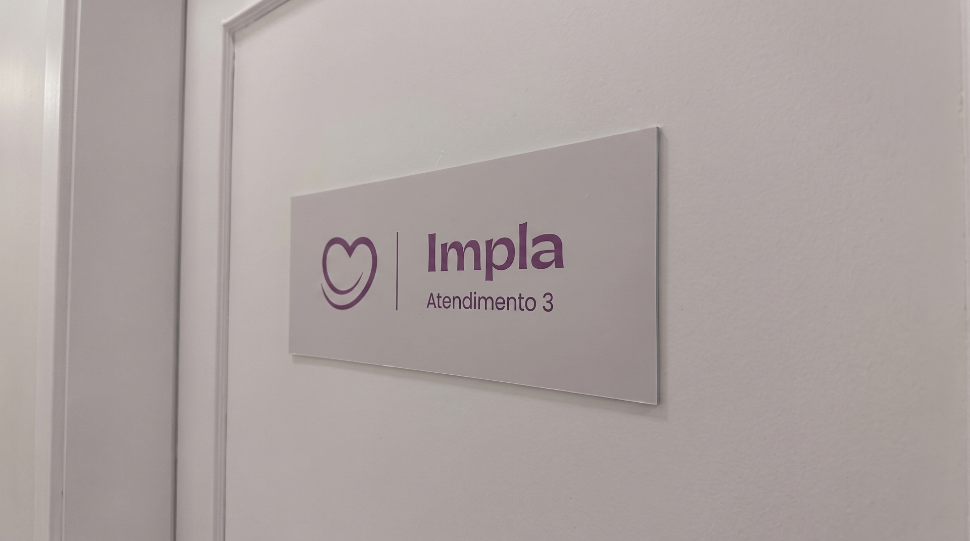 Placa de identificação 'Impla - Atendimento 3' na porta de uma sala da nova unidade da Clínica Impla