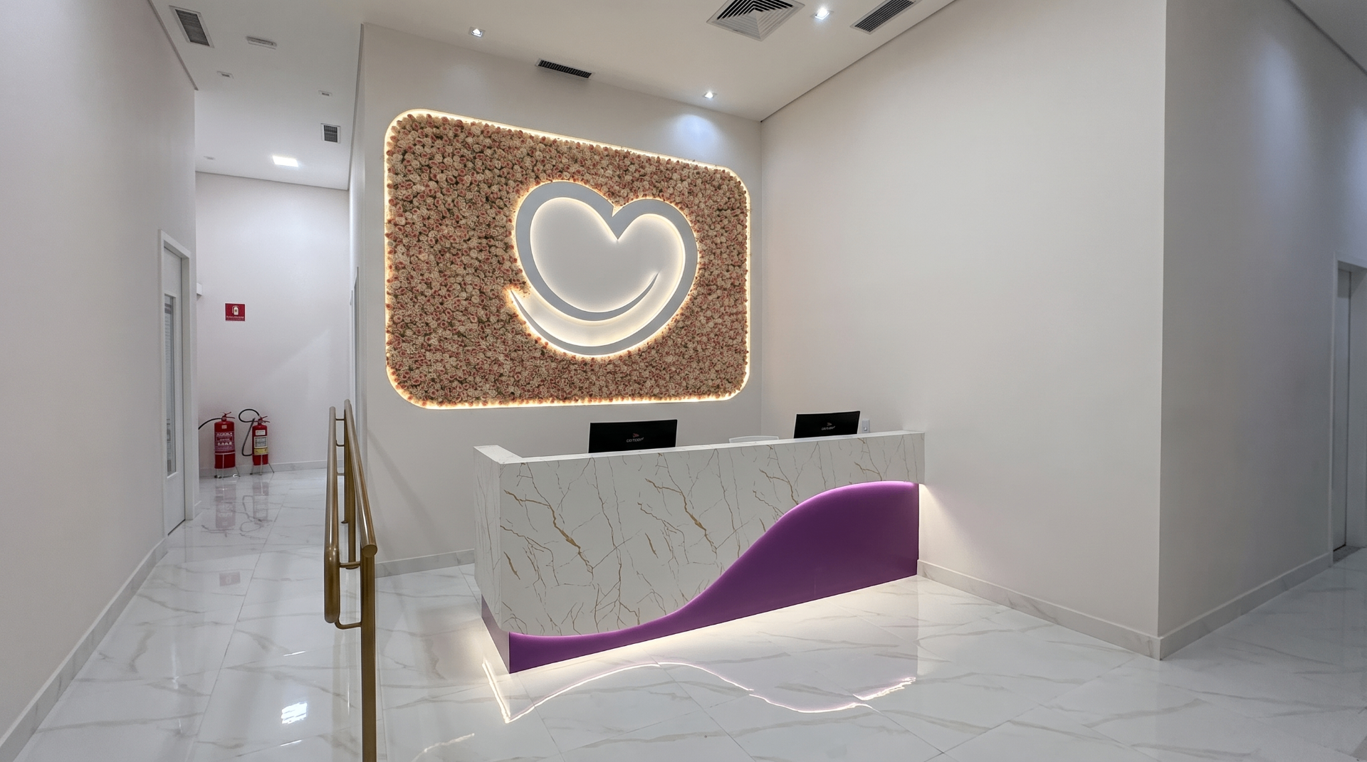 Recepção da Clínica Impla no Shopping Santo Amaro com painel de flores e coração iluminado sobre o balcão de mármore